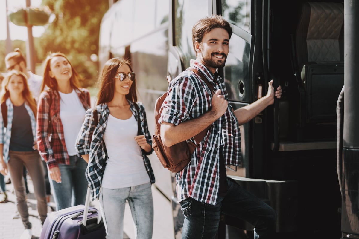 Grupo de jóvenes con equipaje formando fila para abordar un autobús de viaje.