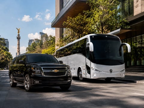 SUV Chevrolet negro y autobús de pasajeros blanco estacionados en calle con monumento visible