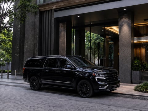 SUV de lujo negro estacionado frente a edificio moderno con columnas oscuras y entrada de vidrio